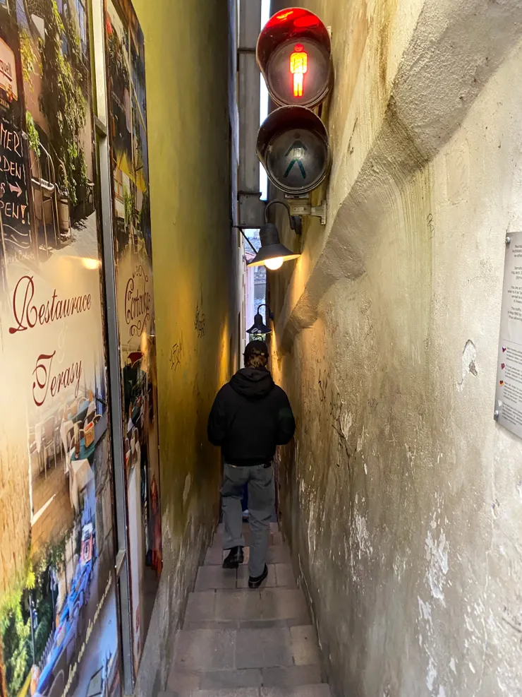 維娜納小巷(Vinarna Certovka),就像是布拉格版的摸乳巷,因為巷道太窄,還在裡頭設置了手動紅綠燈,若某一方有人要通行,便按下號誌鈕。穿過窄巷之後,別有洞天,等著的是一處偌大的露天咖啡店。