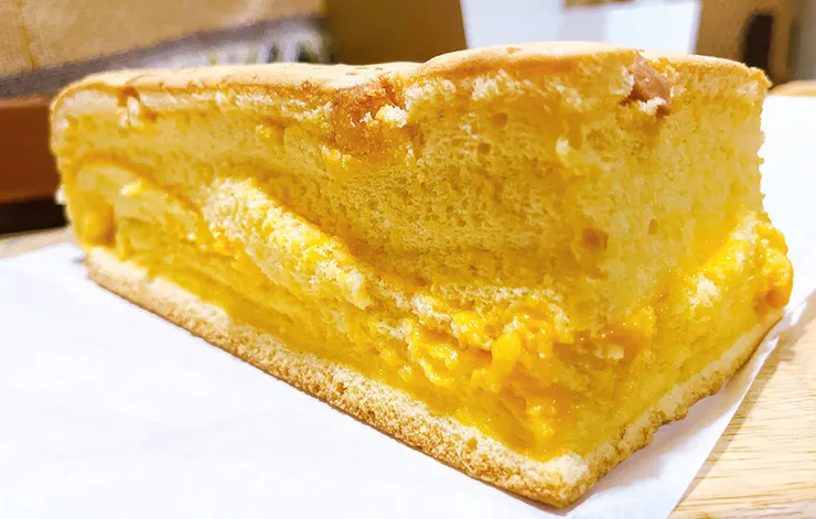 近距離觀察德國起士豆漿蛋糕，展示蛋糕體細緻的孔洞與中心濃郁起士餡的對比，強調其鹹甜適中且濕潤不乾口的絕佳質感。