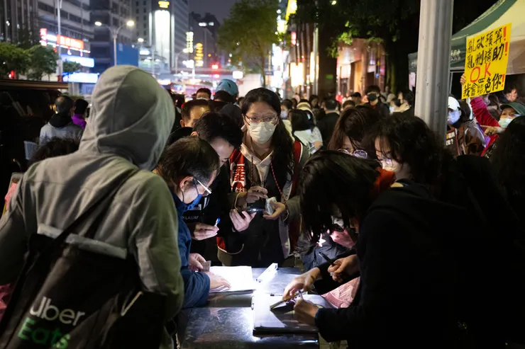 志工團體在夜間街頭收集罷免連署書的景象。一批民眾聚集在攤位前簽署連署，彰顯了此次「大罷免」背後強大的民間動員力量。（攝影／楊子磊；圖片來源／報導者）