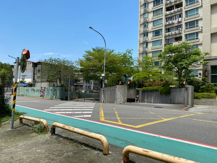 通過興順街，右側是嶄新的大樓，左側則是一排老公寓和一大片停車場。