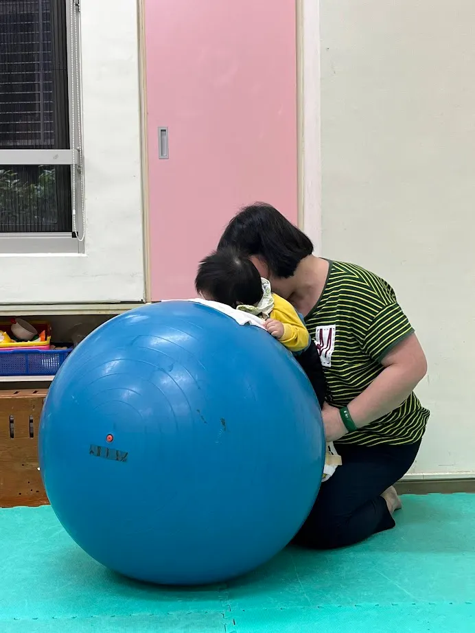 瑜珈球有好多玩法，老師神乎其技地讓孩子覺得舒服又有趣。圖為借助瑜珈球的支撐，小孩能「站」在老師腿上