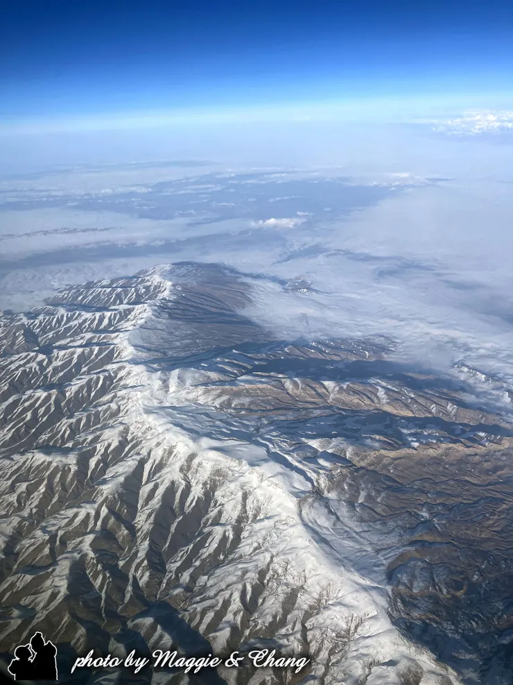 從機窗望出去，一整片雪白山脈如銀龍盤踞大地，遠方是淡淡的雲霧與藍天漸層交織。陽光灑在山脊間，勾勒出層層山勢的立體感，氣勢磅礴卻寧靜悠遠，彷彿置身人間仙境。