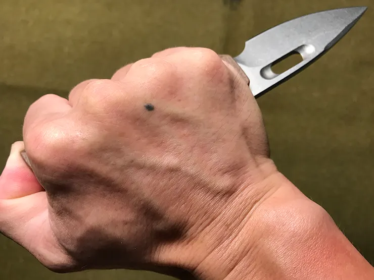 反手戰術持握，刀刃向外，母指抵住柄尾。