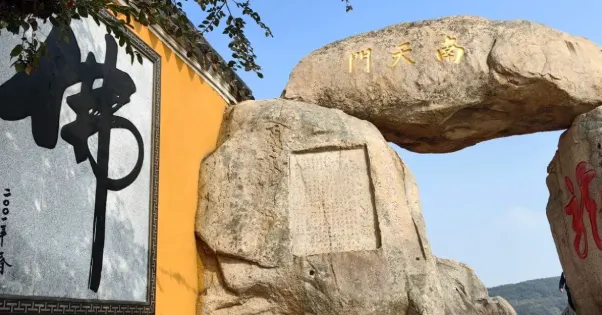 圖片展示了南天門石拱門,拱門上方刻有「南天門」字樣,旁邊是大佛字的石刻,背景則是山景。整體畫面充滿了古老的宗教氛圍,石刻的字體和自然景觀完美融合。