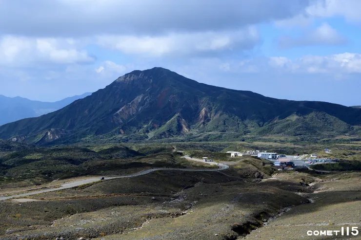 抵達山上公車總站後還要走公園道路（圖左）才能到達火山口，遠方的山峰為烏帽子岳