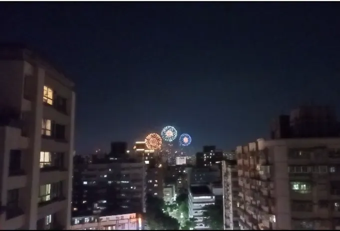 幾棟高樓靜靜立在夜色裡，遠處忽然綻開三朵圓形煙火。  對應那些在不同城市窗邊、樓頂、通勤路上的風鈴與行者——  你或許只覺得自己在黑暗裡趕路，但在別人的視線裡，那一瞬其實是亮起來的信號。