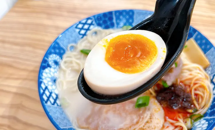 小白拉麵的溏心蛋特寫，剖面展現半熟金黃膏狀的誘人蛋黃，日式拉麵必備靈魂配料。