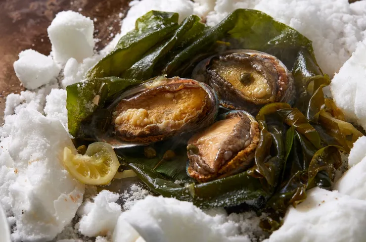 「鹽蒸鮑魚」是  Ukai  鐵板燒料理中傳承逾 40 年的經典招牌菜。以細緻的鹽層包覆鮑魚，以低溫緩慢蒸煮，完整保留海味鮮甜。(圖/ The Ukai Taipei提供)