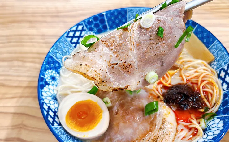 筷子夾起小白拉麵超大片炙燒叉燒，肉質軟嫩且帶有迷人的高溫炙燒焦痕，東湖平價拉麵推薦。