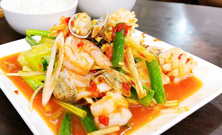 特寫泰式涼拌海鮮，展現鮮艷的洋蔥、香菜與爽口海味食材。
