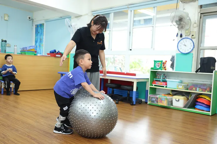 (圖說:教保員利用瑜珈大球,引導小貝推著球行走,藉此增加軀幹與四肢的肌耐力。)