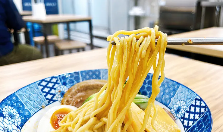 筷子大口夾起小白拉麵沾滿金黃蛋液與醬汁的日本粗麵條，麵體滑潤油亮，極具食慾感。