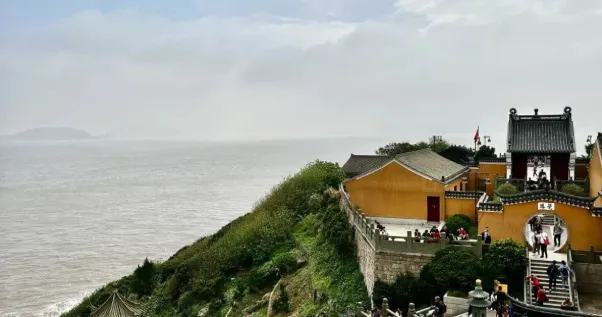 遠處可見海面。廟宇建築古樸,色彩鮮明,周圍綠意盎然。圖片的景致呈現出山與海的美麗結合,增添了詩意的氛圍。