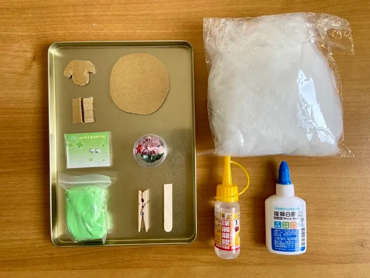 「綿羊MEMO夾」所需材料:綿羊頭、身、腿之造型紙板、綿花、動動眼珠、裝飾用亮片、超輕土、冰棒棍半根及小木夾。另需準備白膠和保麗龍膠來黏貼材料。