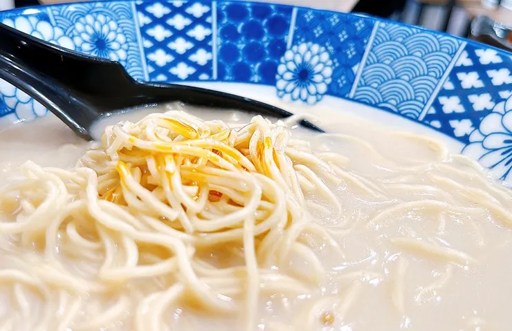 沾滿特製辣油與濃郁蒜味湯汁的拉麵條，紅艷誘人，展現強烈且豐富的味覺衝擊與食慾感。