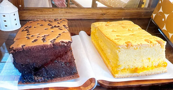 展示兩大塊厚實的現烤蛋糕，左側為表面撒滿巧克力豆且帶有濃郁夾層的限量巧克力口味，右側為夾有鹹甜德國起士內餡的經典口味，質地濕潤綿密。  23.jpg：現場試吃服務