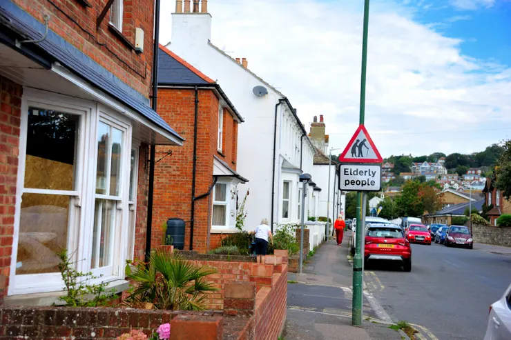 【屋舍各自有型卻又奇妙地統一，聽說房產不便宜大家愛來養老！看這路邊警示牌就知道，而前面也正走著一個老人。
