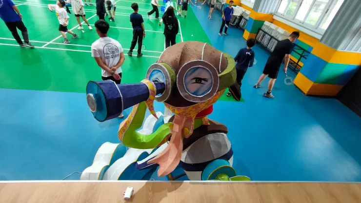 阿蛇繫著紅色長圍巾，長長的蛇身舉著一隻望遠鏡，還戴著一頂大大的飛行帽及風鏡。