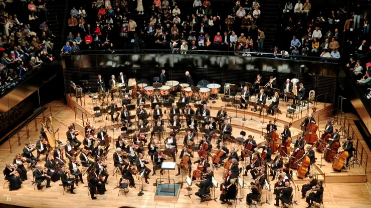【舞台置中座席四周環繞像競技場 百年樂團就位迎進指揮滿座鼓掌！樂團已就位，廳內座無虛席。】