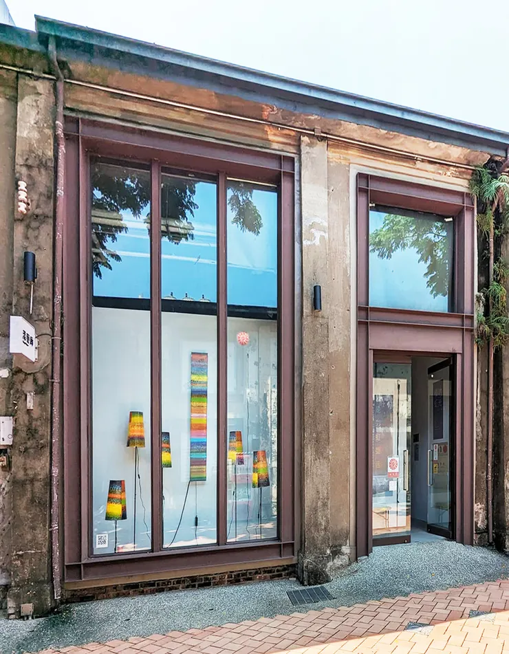 櫥窗設計給人一種溫暖而明亮的感受。色彩豐富的燈具和牆面裝置呈現出彩虹般的層次感,燈光從內部散發,透過透明的玻璃窗傳遞出柔和而溫馨的光線,讓人感到舒適、平靜、希望與多元性的氛圍。(地點:漾藝廊的櫥窗設計與室外大門入口處全景。)