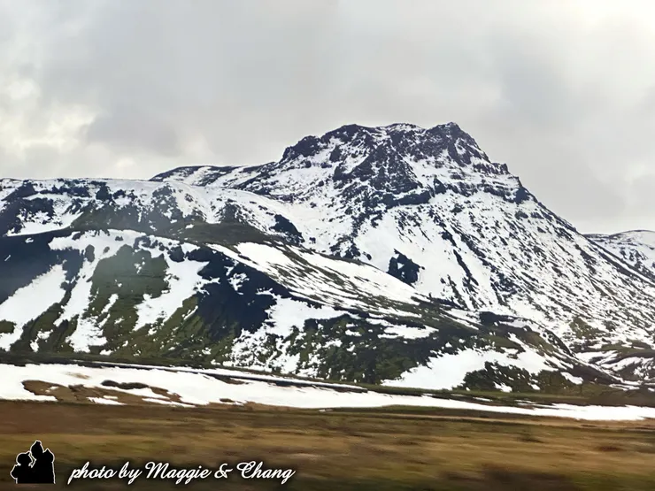 從遊覽車窗拍出去的冰島公路，遠方有白雪覆蓋的山脈，呈現冷色調的純淨美感。