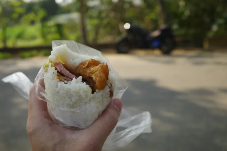 坐在路沿的石墩上，悠閒自在的享用著一個人的飯糰。