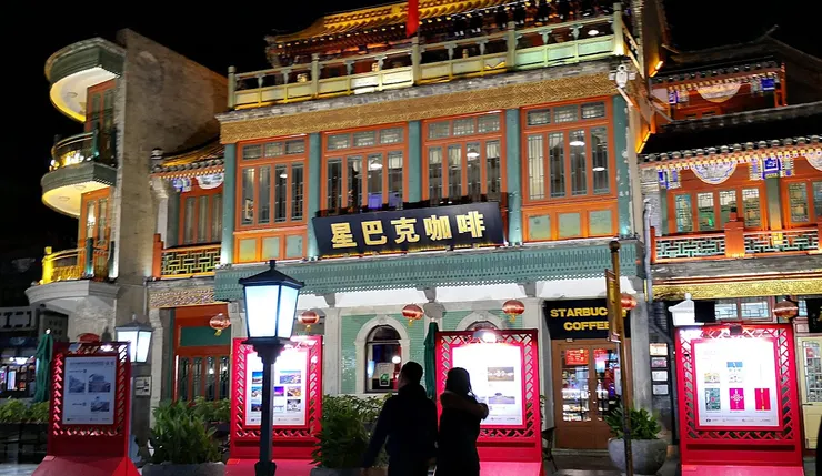 北京的星巴克：青磚牆、綠色廊柱、橙紅木窗與雕花欄杆，搭配夜晚暖光燈籠