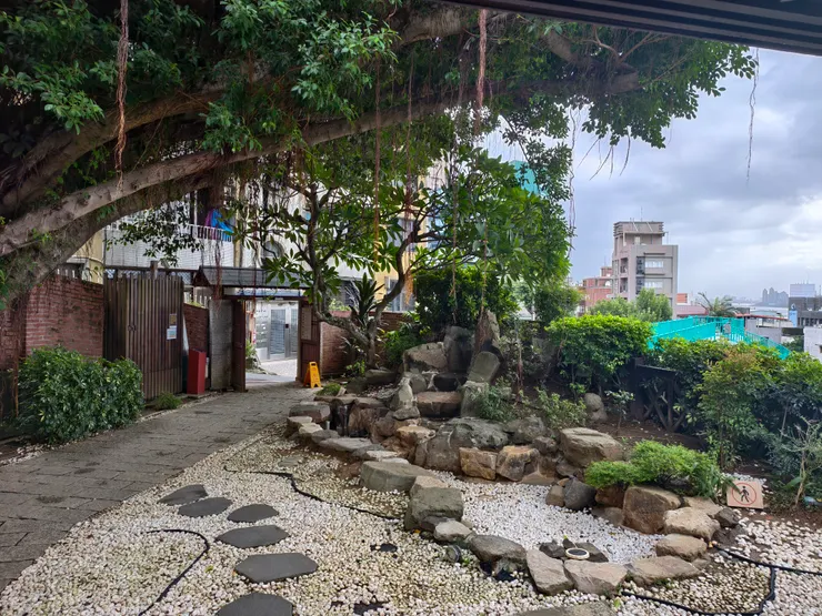 由前緣側觀看前院。前院池塘原有養魚，近來改鋪白色圓石，右邊突兀的綠色柵欄是通往馬偕街的天橋。