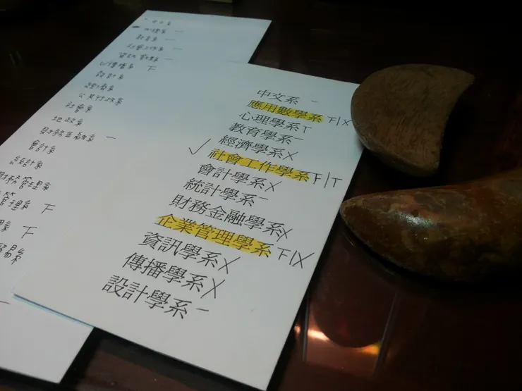 改變我大學就讀科系的擲筊。右邊的紙條是第一次擲筊的結果，是社工系拿下最高票。後來，在我的堅持之下又擲一次，就是左邊寫了二十幾個科系的紙條，但結果沒有鑑別性。在和媽媽討論之後，還是右邊紙條詢問出來的結果為主。