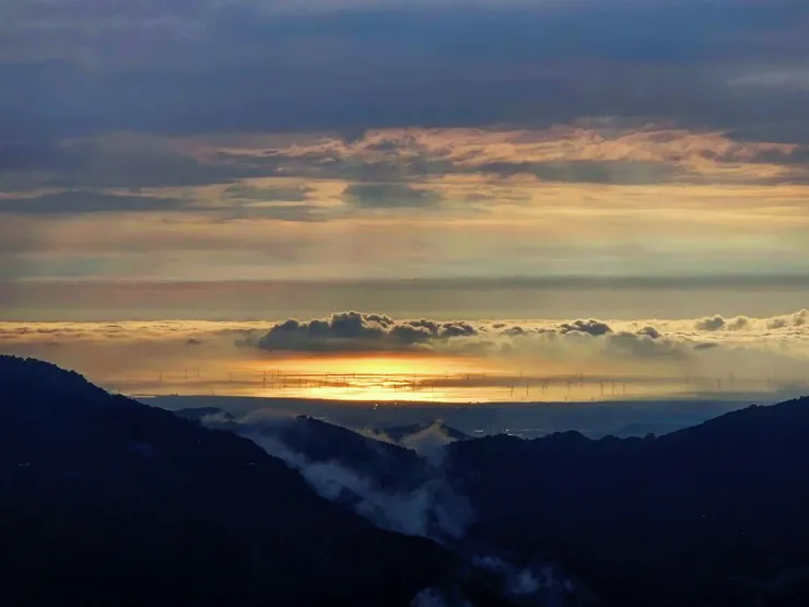 金黃夕陽灑落海洋上，雨後的山嵐雲霧藏在山巒間。
