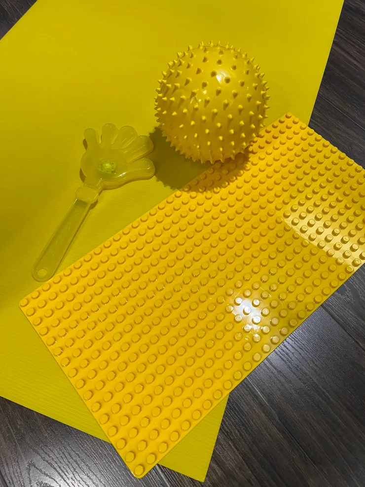 黃色的道具們：塑膠瓦楞板、積木板、觸覺球、會發光的拍拍手。