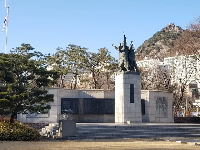 西大門獨立公園內的三一獨立宣言紀念塔。馬路對面的集合式大樓建地，原是「探監巷」所在的傳統街區。