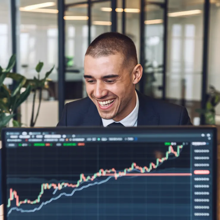 A photo of a cryptocurrency trader with a big smile on his face, as he looks at his computer screen. The screen is displaying a chart with a sharp upward trend. The trader is wearing a suit and tie and has short hair. The background is a modern office with glass walls and a few potted plants.