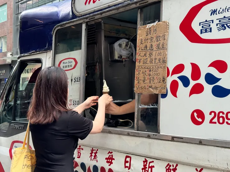  大夥排隊對車窗內的店員點餐，旁邊的簡易看板有說明支付方式：現金、八達通、支付寶、微信。