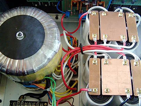 原本是打算將變壓器分開水平擺放,但後來發現會太靠近主線路的 BIAS 板,所以只好把兩顆變壓器疊著固定啦,當時自己弄了這批電容回來時,發現屁股長了一根螺絲,是固定用的,後來有網友告知那根螺絲是和電容的負極導通的,若是在雙橋整流的場合,就不可以一起鎖在導體上。後來只好去切一塊壓克力板,將電容鎖在壓克力板上,再將壓克力板用銅柱墊高,不和機殼直接接觸,以免短路