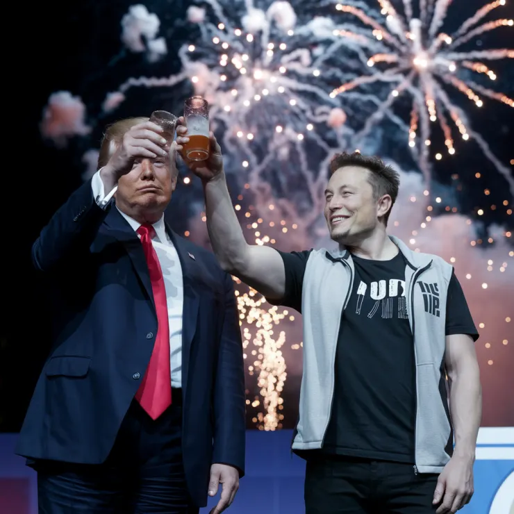 A photo of Donald Trump and Elon Musk raising a toast in a celebration. Trump is wearing a suit and a red tie, while Musk is wearing a black t-shirt and a gray vest. They are standing on a stage. There are fireworks exploding in the sky behind them. The background is dark.