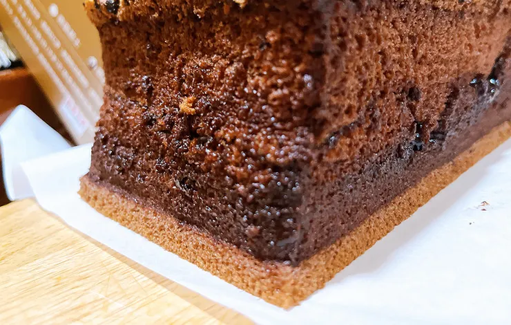 近距離特寫巧克力蛋糕表面，水滴巧克力豆與帶有細微氣孔的巧克力豆漿蛋糕質地完美結合，強調食材的濃郁感與細緻度。