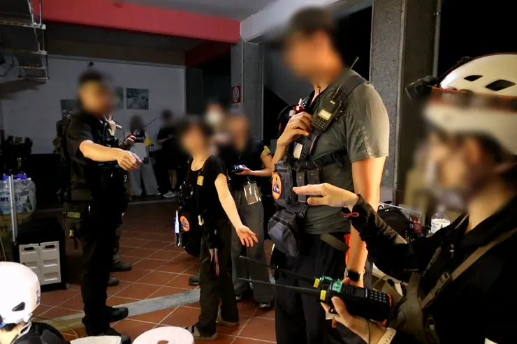 指揮組指揮官正在向各組聯絡官確認狀況；各組聯絡官常要守聽兩組無線電、進行縱向與橫向溝通；畫面外則有記錄組成員記錄所有的回報資訊