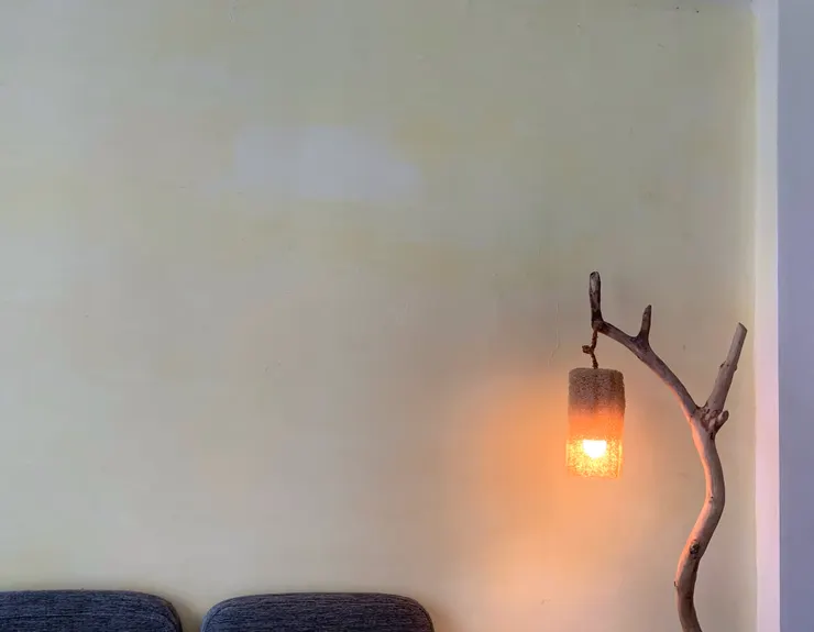 用枯枝做的樹燈擺放在沙發旁，成為一進家門的視覺焦點。燈罩選用絲瓜絡，與後方淡黃底牆面形成柔和舒服的視覺感。