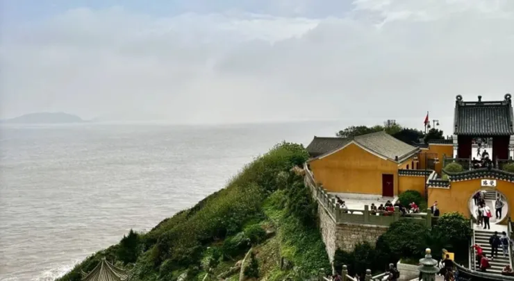 遠處可見海面。廟宇建築古樸，色彩鮮明，周圍綠意盎然。圖片的景致呈現出山與海的美麗結合，增添了詩意的氛圍