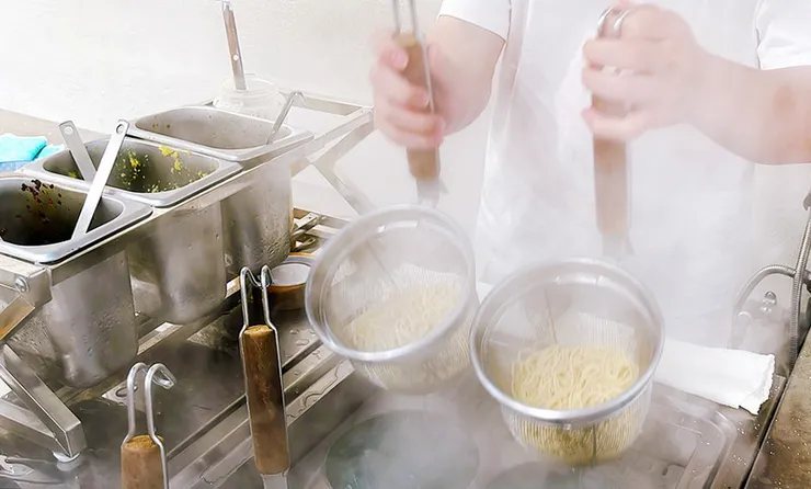 小白拉麵師傅雙手持煮麵網用力甩乾麵條水分的瞬間動作，展現保留拉麵濃郁湯頭與Q彈口感的美味秘訣。