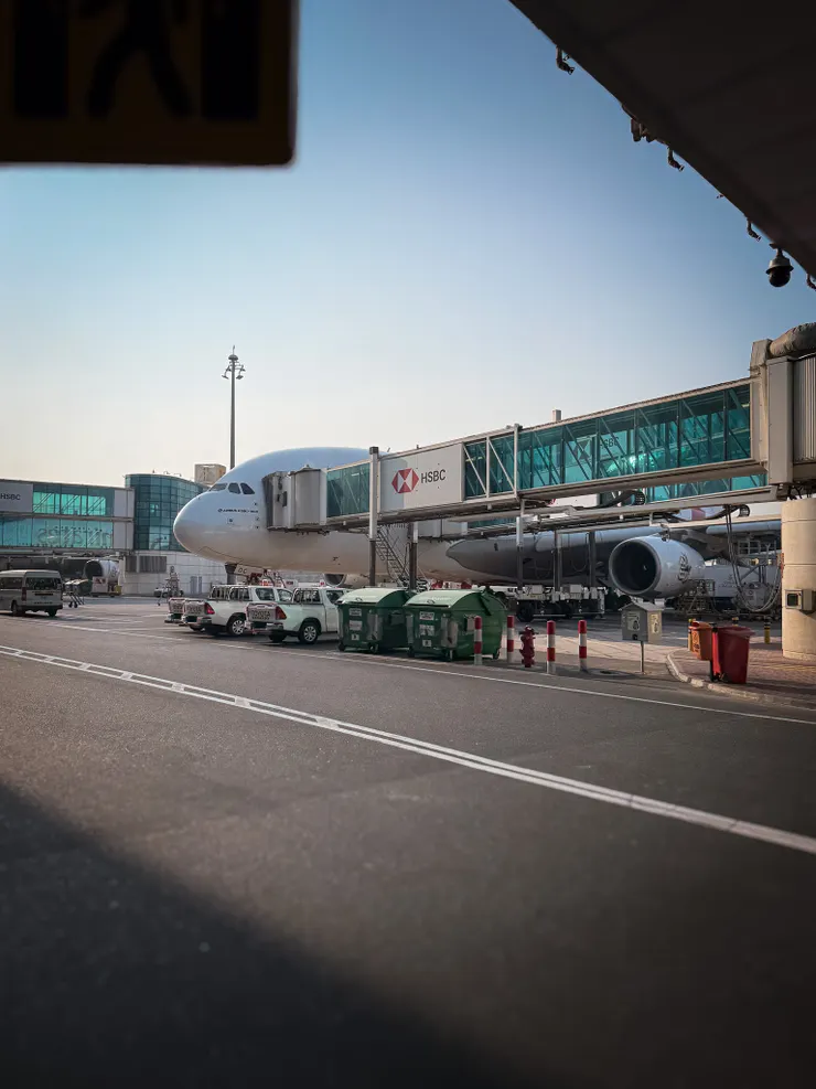 Emirates Airbus A380 at Dubai Airport gate with jet bridge and ground vehicles.