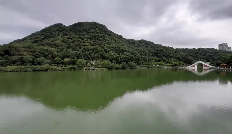 一抹桃紅拱橋浮立在翠綠的湖水上，跨過拱橋連接背後高聳白鷺山，從遠處眺望，拱橋曲線構圖與白鷺山山形呼應。