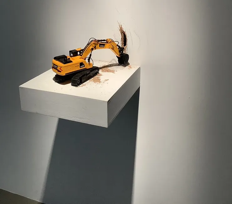 《偽裝—挖土機》玩具挖土機把展牆挖出一個洞。