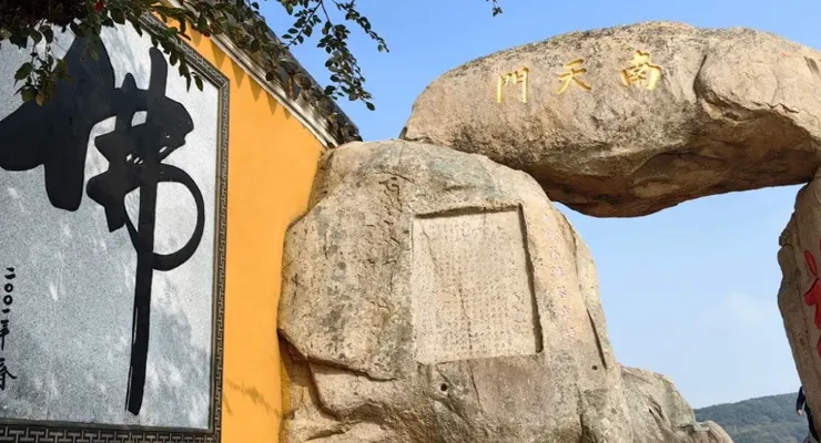 圖片展示了南天門石拱門,拱門上方刻有「南天門」字樣,旁邊是大佛字的石刻,背景則是山景。整體畫面充滿了古老的宗教氛圍,石刻的字體和自然景觀完美融合。