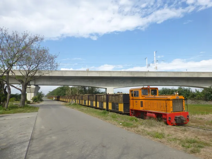 圖示:糖鐵德馬牌柴油火車頭拉裝滿製糖白甘蔗的列車,行駛在雲林虎尾馬公厝線穿越台灣高鐵高架橋。圖片來源為張居隱:https://www.shutterstock.com/zh-Hant/2663705607
