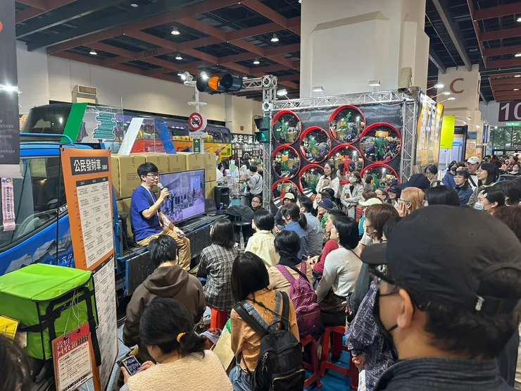 在讀字塞車攤位聽講的人潮，後方可見遊覽車