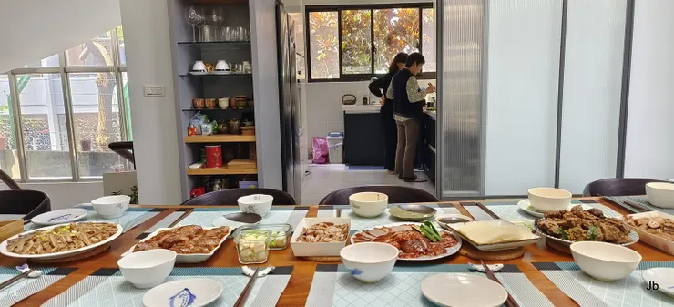 【眾人將帶來的菜擺上桌！廚房裡，雯琦與女主人眼睛在弄湯，窗外變葉木光燦燦。】