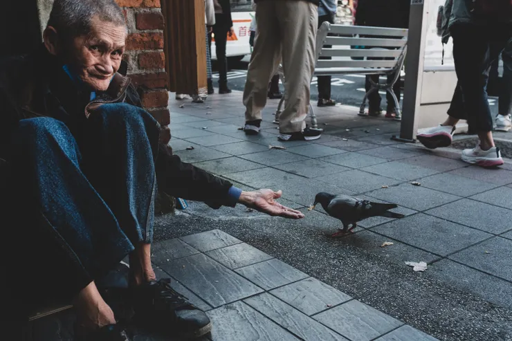 2022年拍攝於雙連站，我不知道他的姓名，但至少一年以下，他都會坐在約莫寶祥銀樓前方，我常常跟他對到眼，偶爾給他零錢，他常常看書，並且多半時候都在看書，偶爾餵餵鴿子，某段時間走路去雙連並且與他點頭問好成為我的日常，終於到某個時刻，我跟他好像達成一種默契，讓我拍攝他餵鴿子的照片。  但2023至今，我沒再看過他，他的位子換成了另一個人，我不知道他去了哪裡，如果再遇到我會送他這張照片吧，順便問一下他平常到底看哪本書。