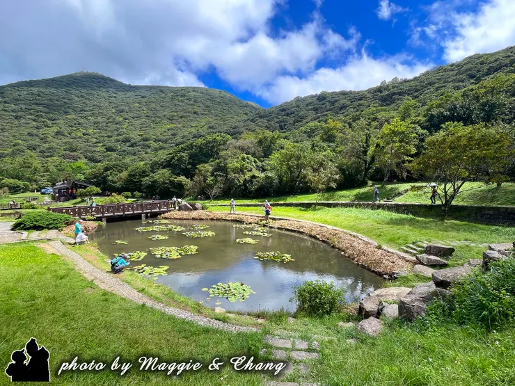 青山環繞的池畔,幾位遊客悠閒地散步或坐在水邊,池中點綴著蓮葉與倒映的藍天。這張照片充滿生機與平和,展現出陽明山的自然生態與悠閒氛圍。